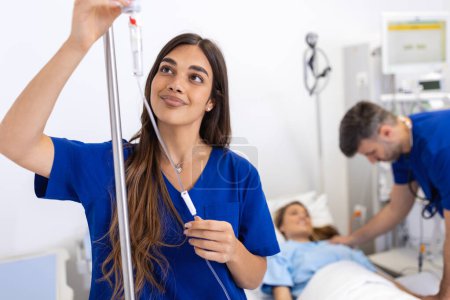 Téléchargez les photos : Jeune femme médecin anesthésiste vêtue de robe bleue, met le compte-gouttes IV dans la chambre d'hôpital - en image libre de droit