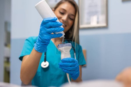 Foto de Médico sonriente que aplica gel en el dispositivo de ultrasonido antes del tratamiento. Las manos en los guantes aplican una tira de gel transparente al sensor ultrasónico del escáner. - Imagen libre de derechos
