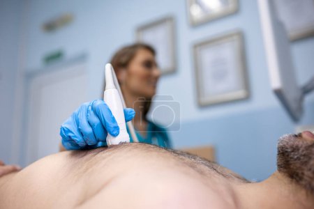 Photo for Female medic using modern ultrasound equipment and examining heart of male patient lying on medical table during diagnostic in hospital - Royalty Free Image