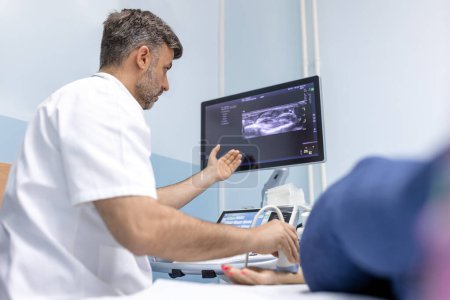 Foto de En la clínica médica, médico varón caucásico que realiza la prueba de ultrasonido doppler de arterias y venas en una paciente femenina - Imagen libre de derechos