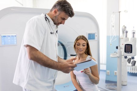 Foto de Paciente femenina que toma asiento y hace preguntas sobre la tomografía computarizada para cultivar médico después del procedimiento de examen en el hospital moderno - Imagen libre de derechos