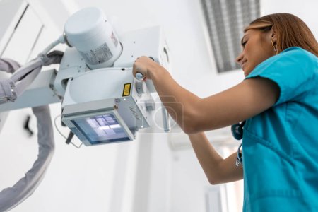 Foto de Doctor mirando la máquina de rayos X en la clínica. La doctora pone la máquina en rayos X sobre el paciente. Radiólogo y paciente en sala de rayos X. - Imagen libre de derechos