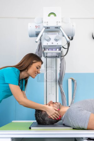 Foto de Paciente masculino sentado mientras enfermera ajustando la moderna máquina de rayos X para escanear su brazo o mano en busca de lesiones y fracturas - Imagen libre de derechos