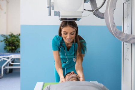 Foto de Paciente masculino acostado en la cama mientras enfermera ajustando la moderna máquina de rayos X para escanear su pecho en busca de lesiones y fracturas - Imagen libre de derechos