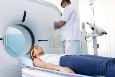 Foto de El paciente se acuesta en una tomografía computarizada o resonancia magnética, la cama se mueve dentro de la máquina, escaneando su cuerpo y cerebro bajo la supervisión de un médico, radiólogo. En un laboratorio médico con equipos de alta tecnología. - Imagen libre de derechos