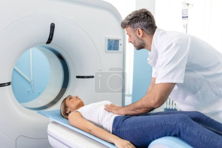 Téléchargez les photos : La patiente se trouve sur un scanner ou une IRM, le lit est déplacé à l'intérieur de la machine, scannant son corps et son cerveau sous la supervision d'un médecin, d'un radiologue. Dans un laboratoire médical avec des équipements de haute technologie. - en image libre de droit