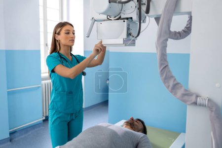 Photo for Female doctor sets up the machine to x-ray over patient. Radiologist and patient in a x-ray room. Classic ceiling-mounted x-ray system. Medical equipment - Royalty Free Image