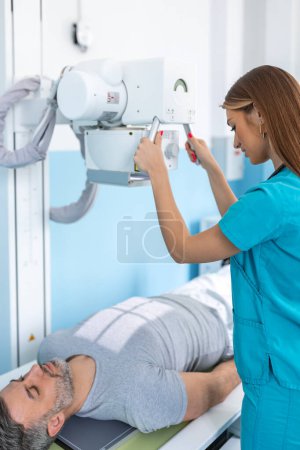 Foto de La doctora pone la máquina en rayos X sobre el paciente. Radiólogo y paciente en una sala de rayos X. Sistema clásico de rayos X montado en el techo. Equipos médicos - Imagen libre de derechos