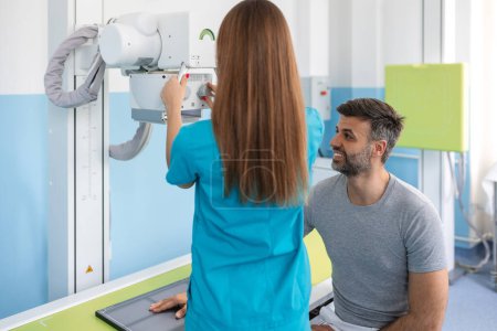 Téléchargez les photos : Radiologiste féminine préparant le patient aux rayons X de la main près de la machine à rayons X. Radiologiste prenant des rayons X du bras des patients - en image libre de droit