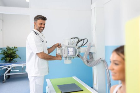 Photo for Radiologist setting up the machine to x-ray female patient. Radiologist and patient in a x-ray room. Classic ceiling-mounted x-ray system. Medical equipment - Royalty Free Image