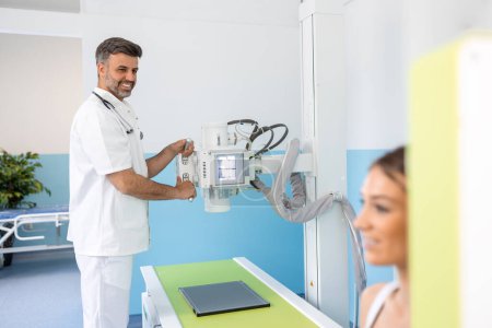 Photo for Radiologist setting up the machine to x-ray female patient. Radiologist and patient in a x-ray room. Classic ceiling-mounted x-ray system. Medical equipment - Royalty Free Image