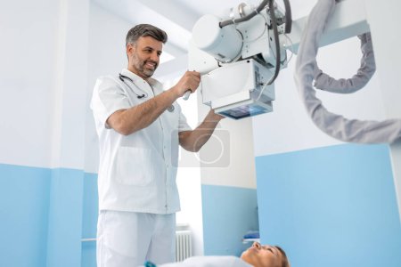 Photo for Multiethnic radiologists with young female patient in x-ray room, Radiologist setting up the machine to x-ray female patient - Royalty Free Image