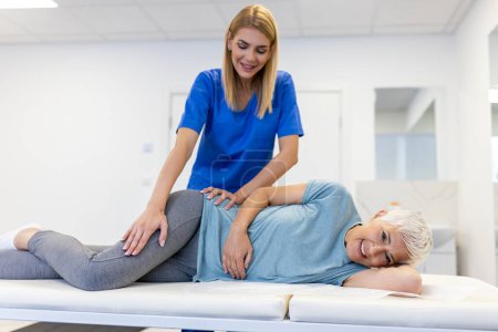 Photo for Young doctor chiropractor or osteopath fixing lying senior woman back with hands movements during visit in manual therapy clinic. Professional chiropractor during work - Royalty Free Image