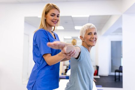 Photo for Doctor orthopedic teaching senior woman to do osteoporosis treatment exercise in modern clinic. Physiotherapist helping female patient during muscle rehabilitation physiotherapy - Royalty Free Image