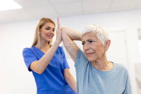 Téléchargez les photos : Médecin orthopédique enseignant aux femmes âgées à faire de l'exercice de traitement de l'ostéoporose dans une clinique moderne. Physiothérapeute aidant la patiente pendant la physiothérapie de réadaptation musculaire - en image libre de droit