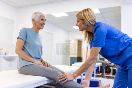 Téléchargez les photos : Orthopédiste professionnel examinant la jambe d'une patiente âgée à la clinique. physiothérapeute faisant la procédure de réadaptation à la femme âgée sur la table de massage. - en image libre de droit
