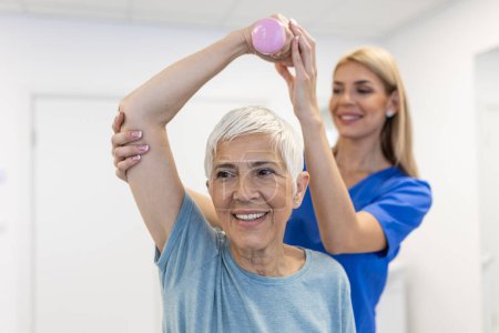 Téléchargez les photos : Physiothérapeute femme donnant de l'exercice avec traitement haltère À propos du bras et de l'épaule de la patiente âgée Concept de physiothérapie - en image libre de droit