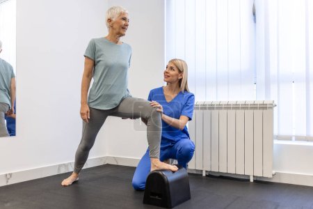 Téléchargez les photos : Patiente âgée à la physiothérapie faisant des exercices physiques avec son thérapeute, faisant de la physiothérapie des jambes pour les femmes âgées, pour traiter l'arthrose et les douleurs nerveuses dans la jambe. - en image libre de droit