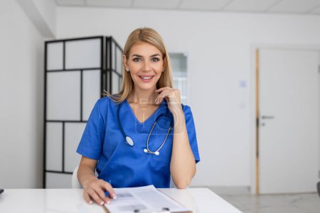 Téléchargez les photos : Portrait d'une jeune femme médecin assise dans un bureau de clinique, remplissant un formulaire médical à table. - en image libre de droit
