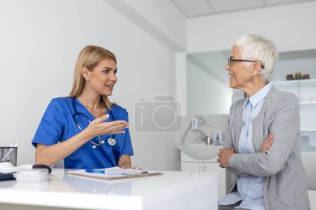 Photo for Young woman doctor or GP in white medical uniform consult senior female patient in private hospital. Female therapist speak talk with woman client on consultation in clinic. - Royalty Free Image