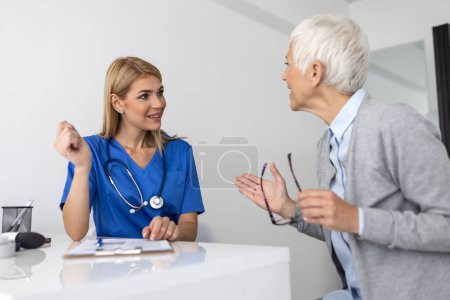 Photo for Young woman doctor or GP in white medical uniform consult senior female patient in private hospital. Female therapist speak talk with woman client on consultation in clinic. - Royalty Free Image