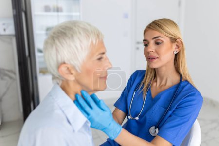 Friendly woman doctor wearing gloves checking sore throat or thyroid glands, touching neck of senior female patient visiting clinic office. Thyroid cancer prevention concept