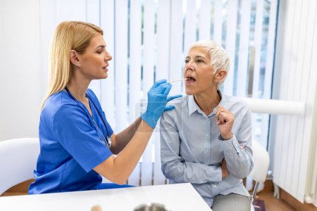 Téléchargez les photos : Une patiente âgée ouvre la bouche pour que le médecin regarde dans sa gorge. Médecin féminin examinant le mal de gorge du patient à la clinique. Otolaryngologue examine le mal de gorge du patient. - en image libre de droit