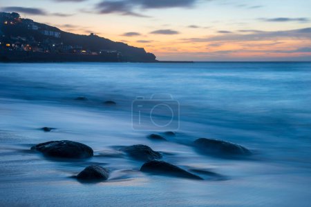 Téléchargez les photos : Beau paysage de Sennen Cove en Cornouailles pendant le coucher du soleil avec un ciel lunaire et une longue exposition au mouvement de la mer - en image libre de droit
