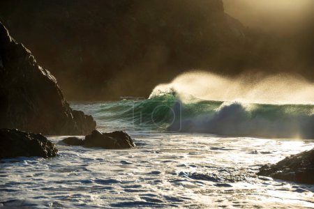 Téléchargez les photos : Image de paysage épique de vagues de jade turquoise s'écrasant sur le rivage et les rochers de Kynance Cove Cornwall avec un fond de lever de soleil éclatant et des gouttelettes d'eau pulvérisées dans le vent - en image libre de droit