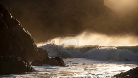 Téléchargez les photos : Image de paysage épique de vagues de jade turquoise s'écrasant sur le rivage et les rochers de Kynance Cove Cornwall avec un fond de lever de soleil éclatant et des gouttelettes d'eau pulvérisées dans le vent - en image libre de droit