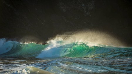 Photo for Epic landscape image of jade turquoise waves crashing onto shore and rocks in Kynance Cove Cornwall with glowing sunrise background and water spray droplets in wind - Royalty Free Image