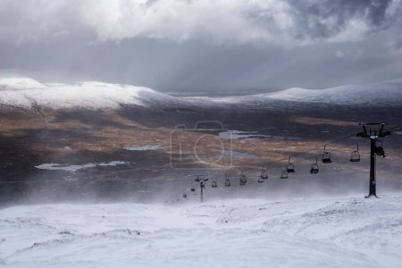 Foto de Hermosa imagen de paisaje de invierno desde la cima de la montaña en las Highlands escocesas hacia Rannoch Moor durante la tormenta de nieve y la deriva de la cima de la montaña en los fuertes vientos - Imagen libre de derechos