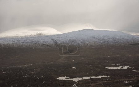 Foto de Hermosa imagen de paisaje de invierno desde la cima de la montaña en las Highlands escocesas hacia Rannoch Moor durante la tormenta de nieve y la deriva de la cima de la montaña en los fuertes vientos - Imagen libre de derechos