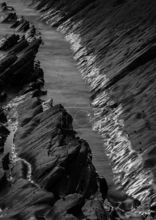 Téléchargez les photos : Image abstraite du paysage de rochers sur Welcome Mouth Beach au coucher du soleil avec des marques de marée sur les rochers réfléchissant la lumière du soleil - en image libre de droit