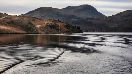 Foto de Beautiful Winter landscape image viewed from boat on Ullswater in Lake District with unusual water ripple wake movements - Imagen libre de derechos