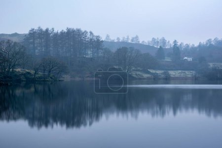 Téléchargez les photos : Belle image de paysage d'hiver de Loughtrigg Tarn par matin brumeux avec de l'eau calme et campagne brumeuse en arrière-plan - en image libre de droit