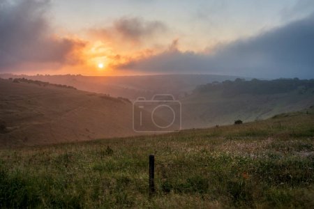 Téléchargez les photos : Incroyable lever de soleil d'été de la digue du diable dans le parc national de South Downs dans la campagne anglaise avec des nuages bas donnant un sentiment d'humeur - en image libre de droit