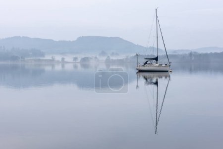 Téléchargez les photos : Superbe image paisible du paysage brumeux du matin de printemps sur Windermere dans le Lake District avec des bateaux amarrés sur le lac et des sommets brumeux lointains - en image libre de droit