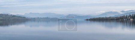 Foto de Impresionante imagen de paisaje tranquilo de brumosa mañana de primavera sobre Windermere en Lake District con barcos amarrados en el lago y picos brumosos distantes - Imagen libre de derechos