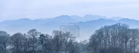 Foto de Impresionante imagen de paisaje tranquilo de brumosa mañana de primavera sobre Windermere en Lake District con barcos amarrados en el lago y picos brumosos distantes - Imagen libre de derechos