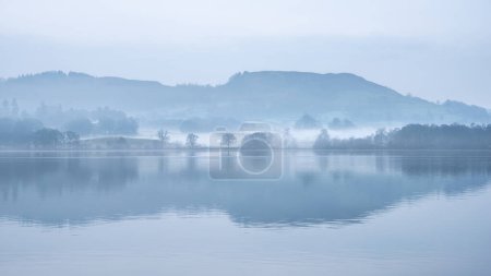 Atemberaubende friedliche Landschaft Bild des nebligen Frühlingsmorgens über Windermere im Lake District mit Booten am See und entfernten nebligen Gipfeln vertäut