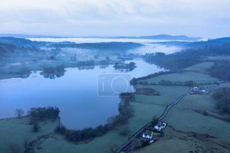 Stunning drone aerial landscape image of cloud inversion around Esthwaite Water in Lake District during Spring sunrise blue hour