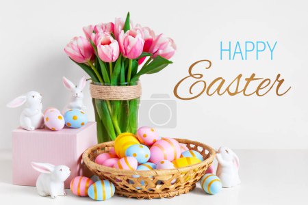 Photo for Easter and spring holiday greeting card concept. Pink tulips, easter bunnies with colorful eggs in basket. Painted Easter eggs in nest and tulips with white bunny. - Royalty Free Image