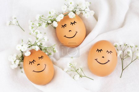 Photo for Three happy Easter eggs with cute faces in floral wreath crowns on white background. Easter eggs with flowers and sleepy eyes in sunny light. Happy Easter concept. - Royalty Free Image