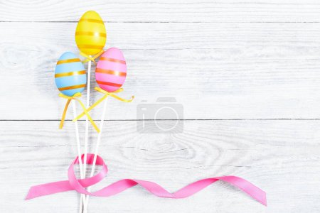 Photo for Three colorful Easter egg with pink ribbon bow on blue old wooden table. Light blue Easter background and copy space. Modern greeting card for the celebration of Easter. - Royalty Free Image
