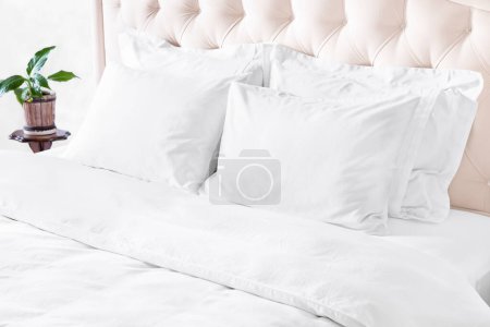Photo for Bedroom with bed, white bedding, and bedside table. White pillows, duvet and duvet case on bed with beige headboard.  Bed with clean white pillows and bed sheets in beautyful bedroom. - Royalty Free Image
