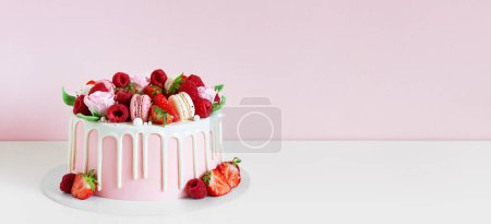 Photo for Panorama of birthday sweet cake with berries, macaron and floral decor on table. Beautiful pink cake decorated with macarons, raspberries, strawberries and sugar rose flowers. Confectionery background with copy space. - Royalty Free Image