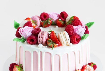 Photo for Birthday sweet cake with berries, macaron and floral decor on table. Beautiful pink cake decorated with macarons, raspberries, strawberries and sugar rose flowers. Confectionery background with copy space. - Royalty Free Image