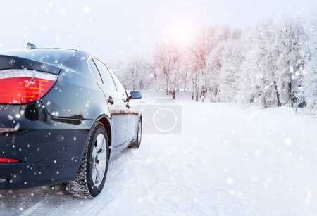 Téléchargez les photos : Voiture noire sur une route d'hiver dans une forêt enneigée, voyage d'hiver. Voiture moderne avec pneus d'hiver sur route enneigée - en image libre de droit