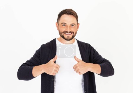 Foto de Joven hombre guapo con barba vistiendo ropa casual sobre un fondo blanco, aprobando hacer gesto positivo con la mano, pulgares hacia arriba. Hombre sonriente y feliz por el éxito. Gesto del ganador. - Imagen libre de derechos